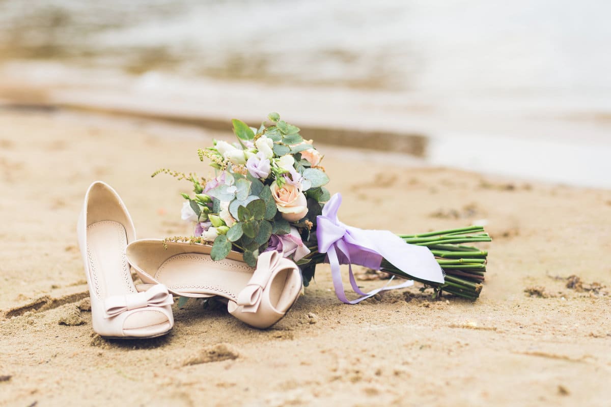 Des chaussures de mariage et un bouquet de mariée sur la plage